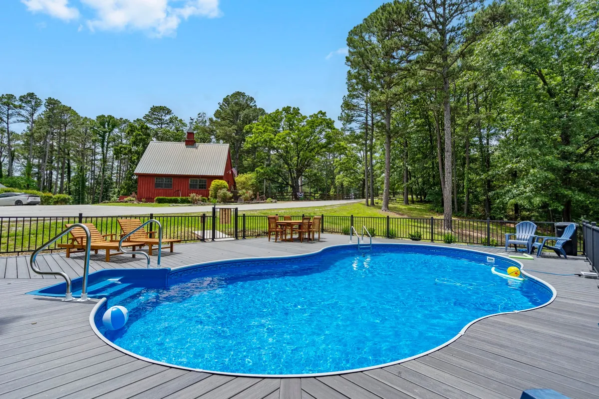 A sparkling swimming pool is set beside a charming red barn and surrounded by towering trees and comfortable deck furniture. The space is tailored for sunbathing, swimming, and relaxed social gatherings, providing a true resort-style experience within a private, community setting.