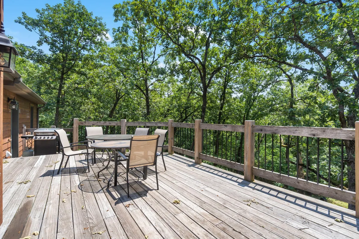 This image presents an inviting outdoor dining table surrounded by lush trees, with a grill visible nearby. The tranquil woodland setting is perfect for both barbecuing and relaxing meals al fresco, directly connecting the indoor living space to the beauty of nature.