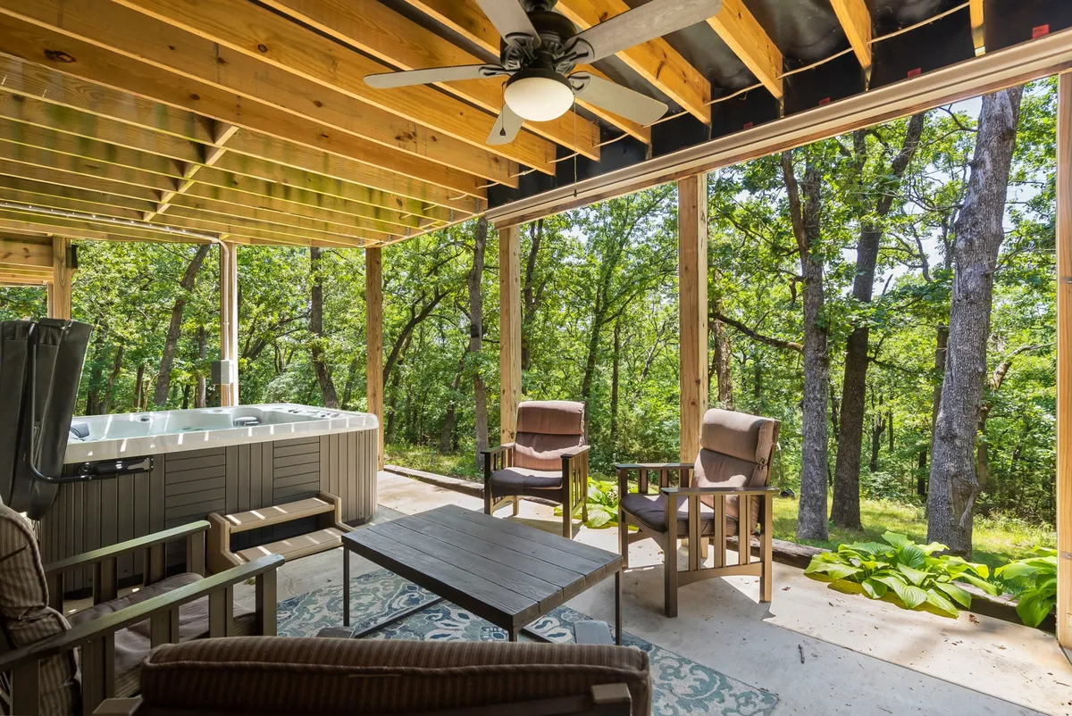 An exterior shot of the covered patio with a bubbling hot tub surrounded by nature. The wooden ceiling overhead and outdoor seating area create a tranquil spot for unwinding after a day of activities, perfectly connecting indoor recreation with outdoor relaxation.