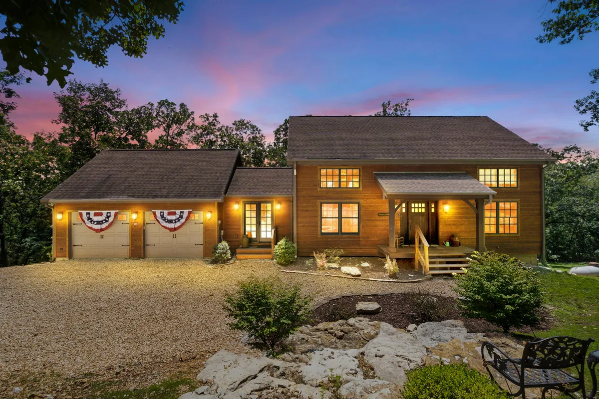 A broad view of the property’s exterior, highlighting large front windows, a decorative porch, and beautifully landscaped gardens. The windows and porch showcase the seamless integration of indoor and outdoor living spaces, ideal for enjoying nature and relaxation.