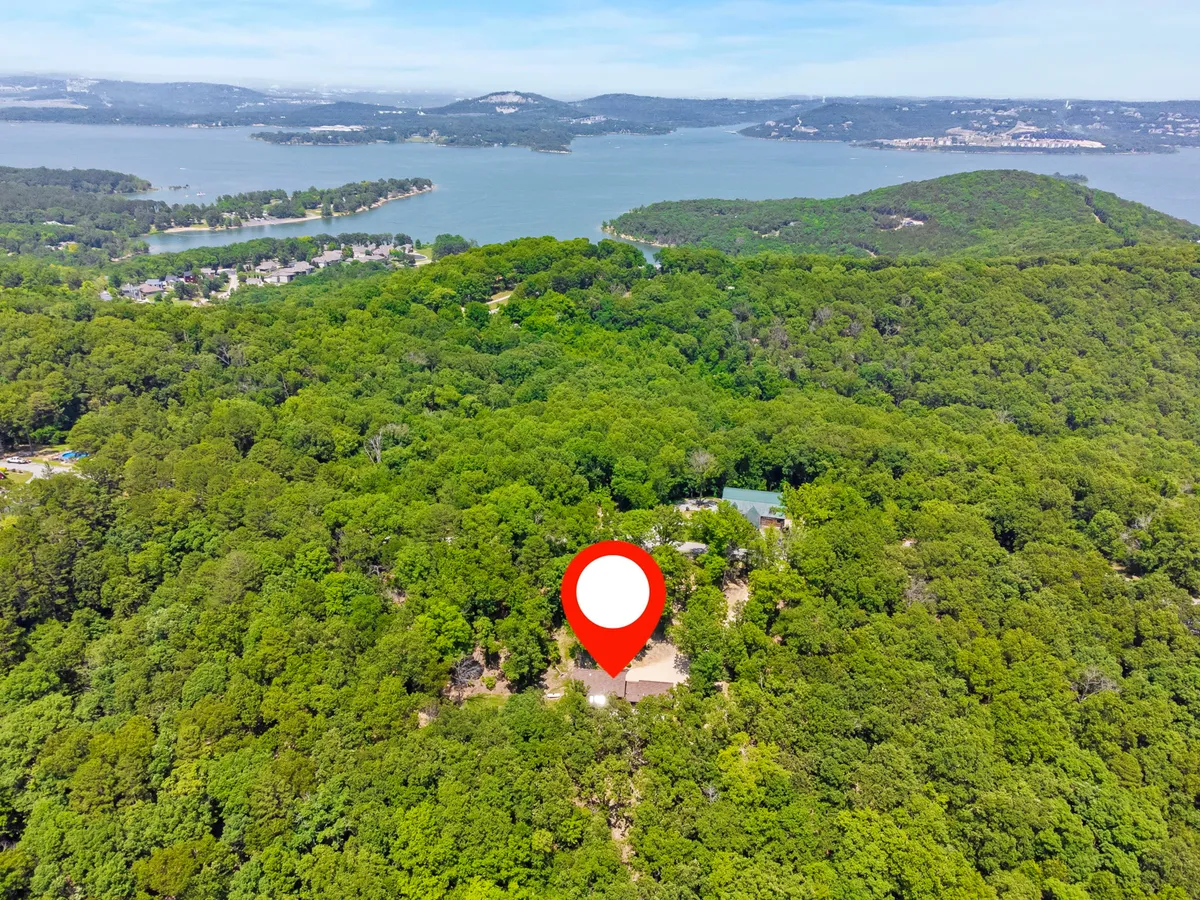 This image captures a panoramic view of lush greenery, a distant lake, and an isolated property nestled in the Ozark landscape. The peaceful, open expanse sets a tranquil mood and suggests abundant opportunities for wildlife observation, hiking, and stargazing.