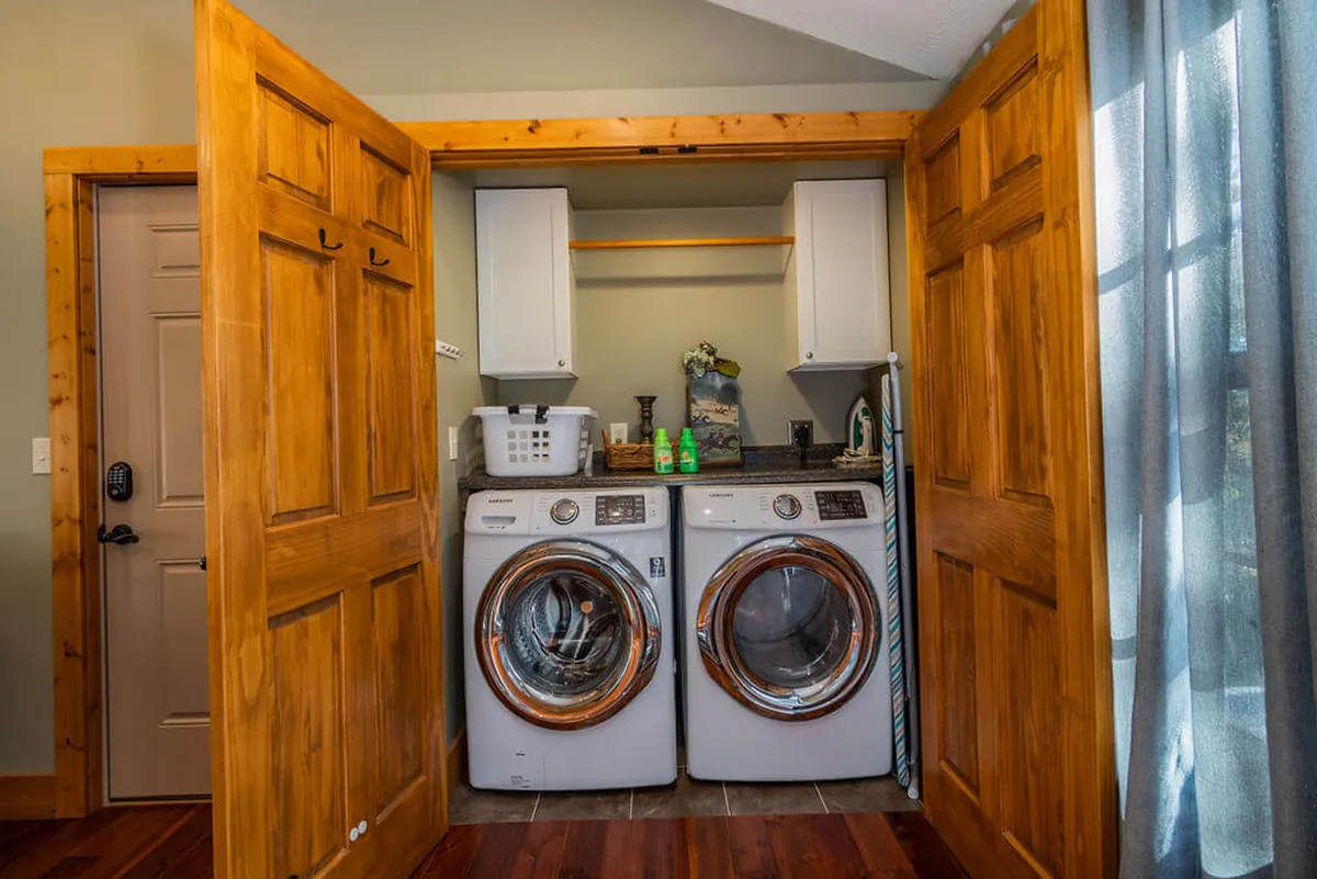 A practical and tidy laundry room featuring a washer and dryer, wooden doors, a shelving unit for supplies, and a clean, organized setup. The mood is efficient yet homey, ensuring guests can easily manage laundry during their stay.