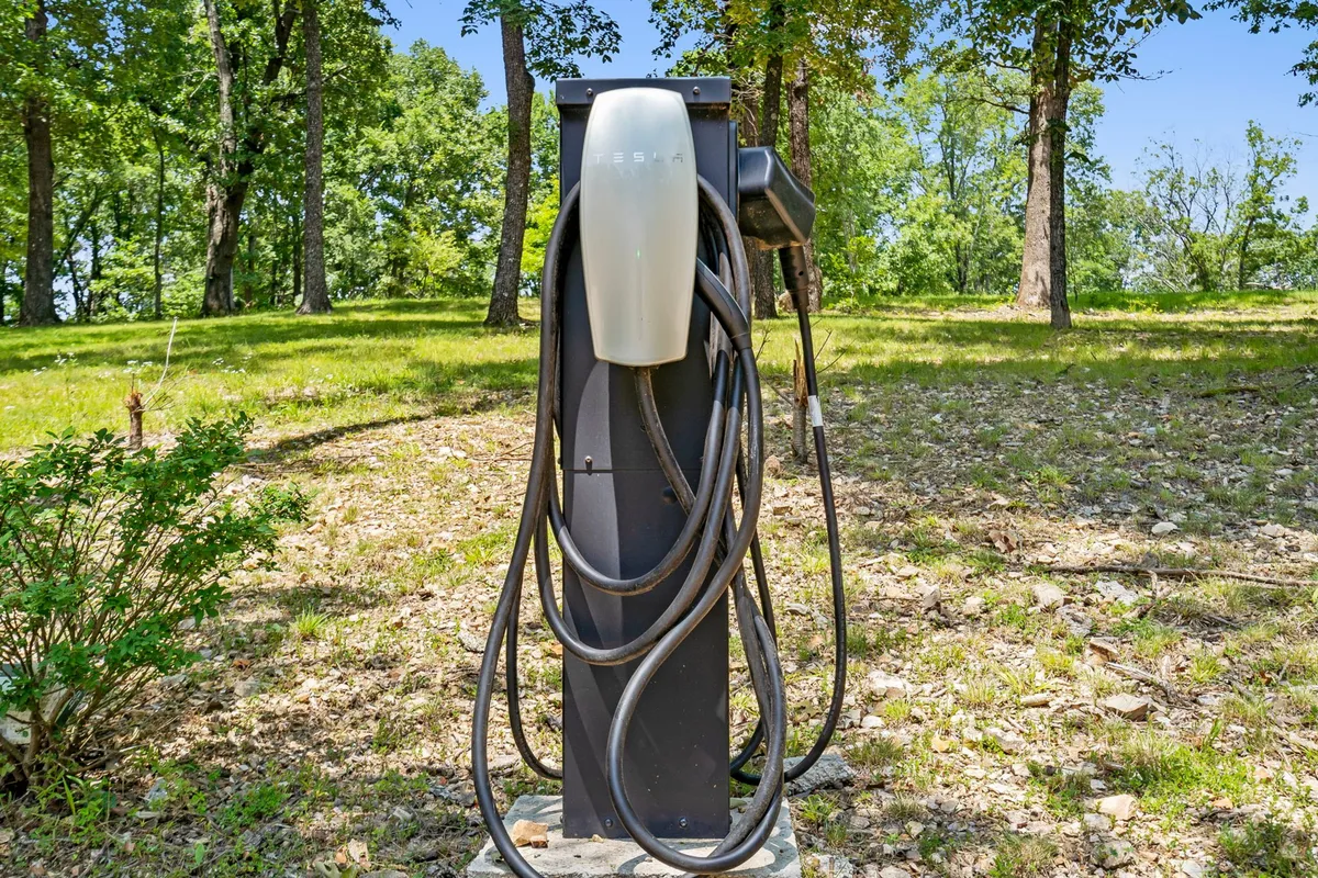 A Tesla charging station stands in a peaceful, green setting, ready to accommodate electric vehicles. The modern charger is juxtaposed with the natural backdrop, symbolizing eco-friendliness and convenience for guests.