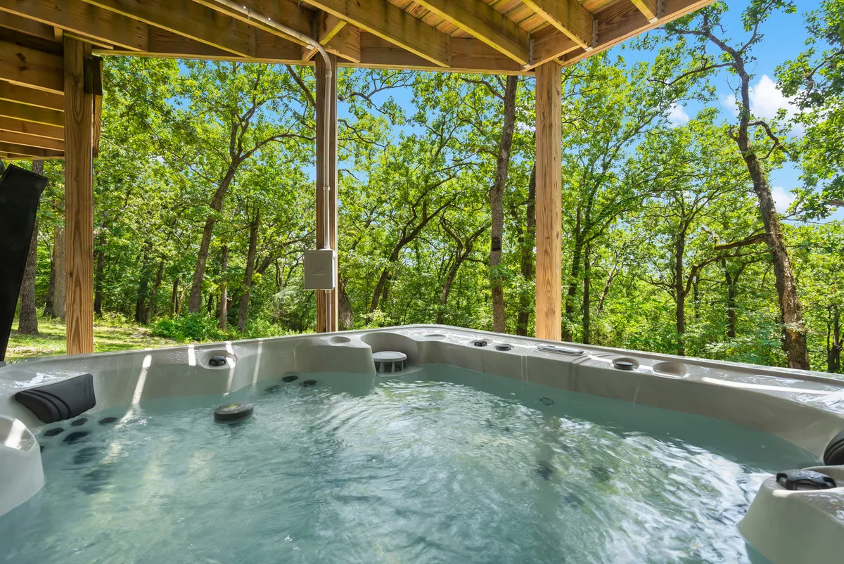 An exterior scene featuring a hot tub on the deck surrounded by tall trees, inviting guests to relax in a tranquil, natural setting. The area is ideal for stargazing at night or enjoying a peaceful soak after a day of exploration.