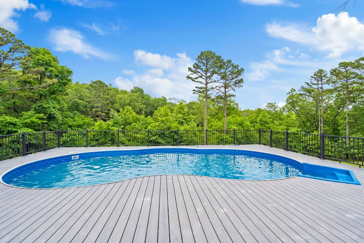 This image features a sparkling swimming pool surrounded by lush greenery and a wooden deck, offering ample space for sunbathing and outdoor gatherings. The pool area is inviting and speaks to relaxation and group fun in a resort-style setting.